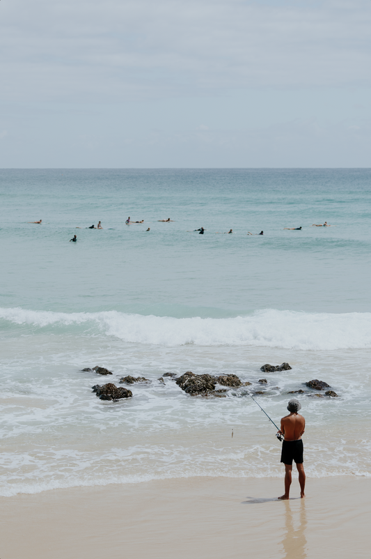 Australian Prints by Mackenzie Sweetnam. A fisherman stands empty handed looking out at the surfers.